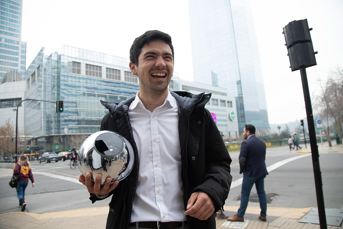 A man joyfully holds an Orb in a city setting, with buildings in the background and people walking nearby.