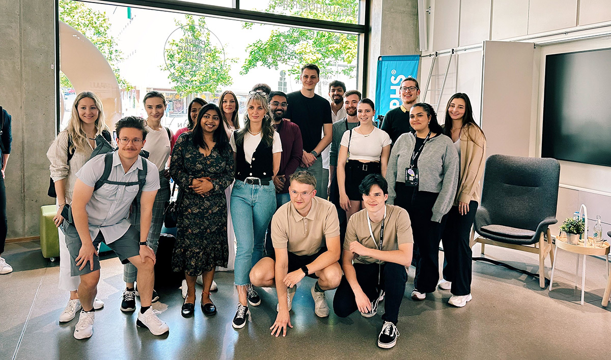 A diverse group of people gathered together, smiling and posing for a group photo in a bright and modern space. Some individuals are wearing casual outfits, while others are more formally dressed. They appear to be celebrating a milestone or event together.