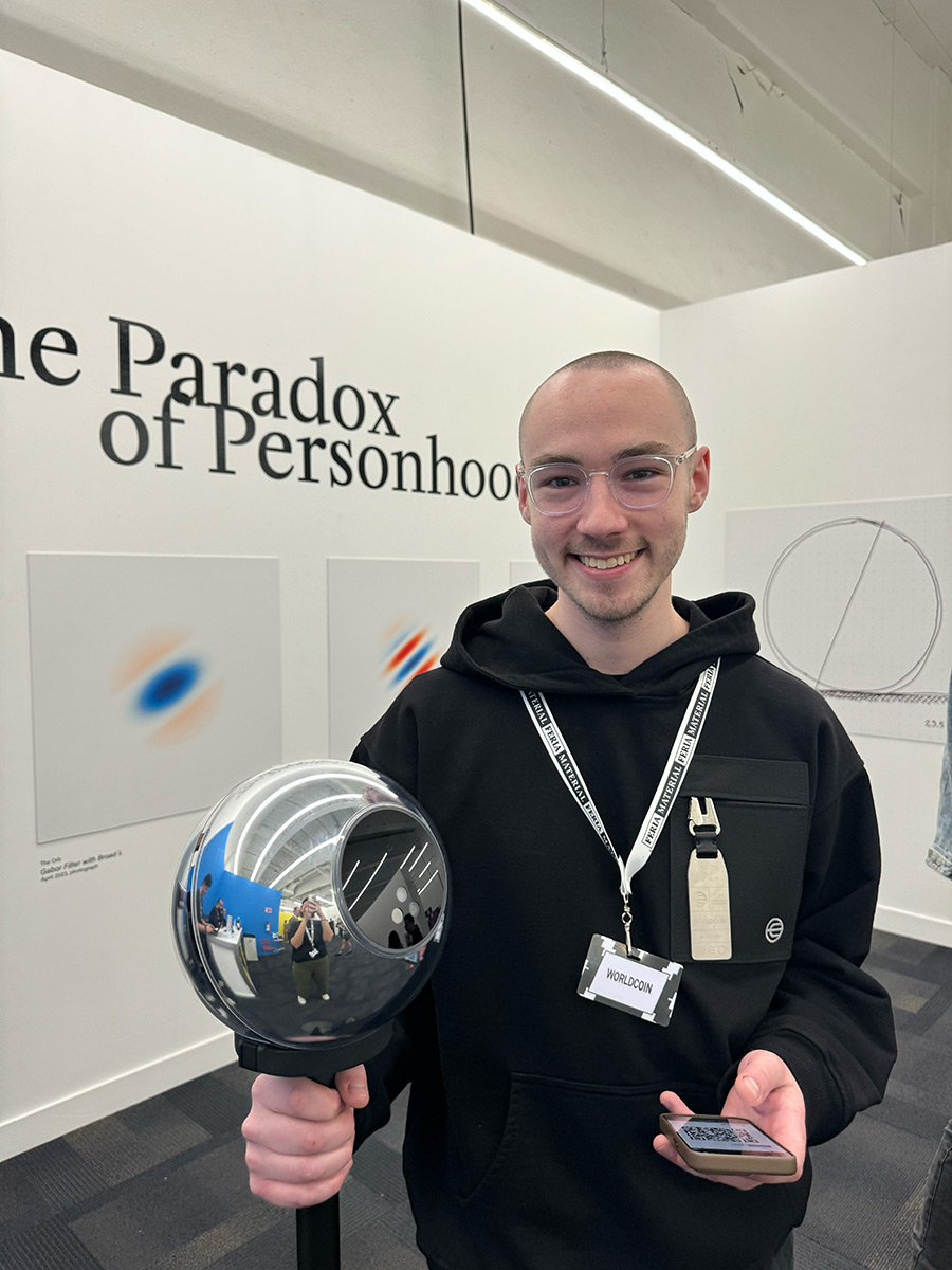 A person smiling and holding the Orb while standing in an exhibition space labeled 'The Paradox of Personhood'.