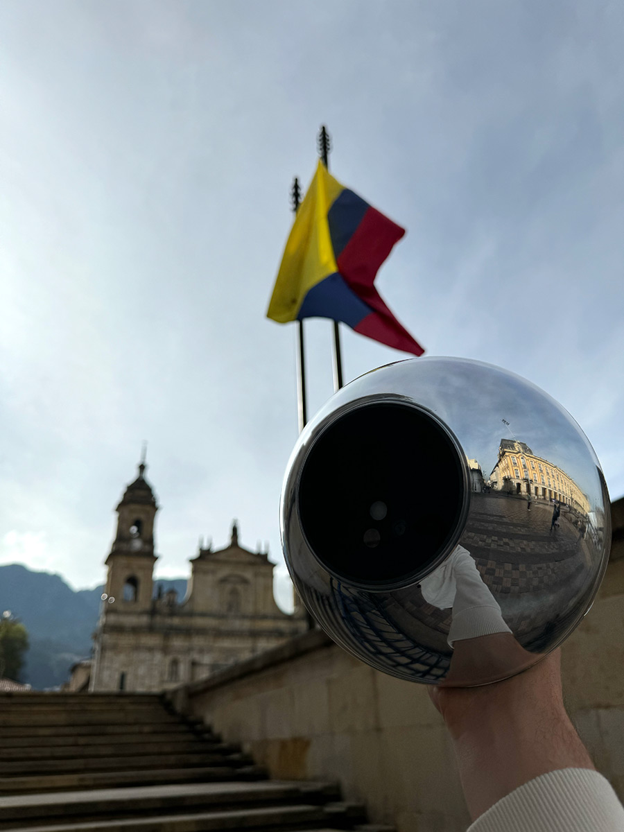 A shiny Orb held in the foreground reflecting a Colombian flag and historical buildings in the background, symbolizing community and innovation.