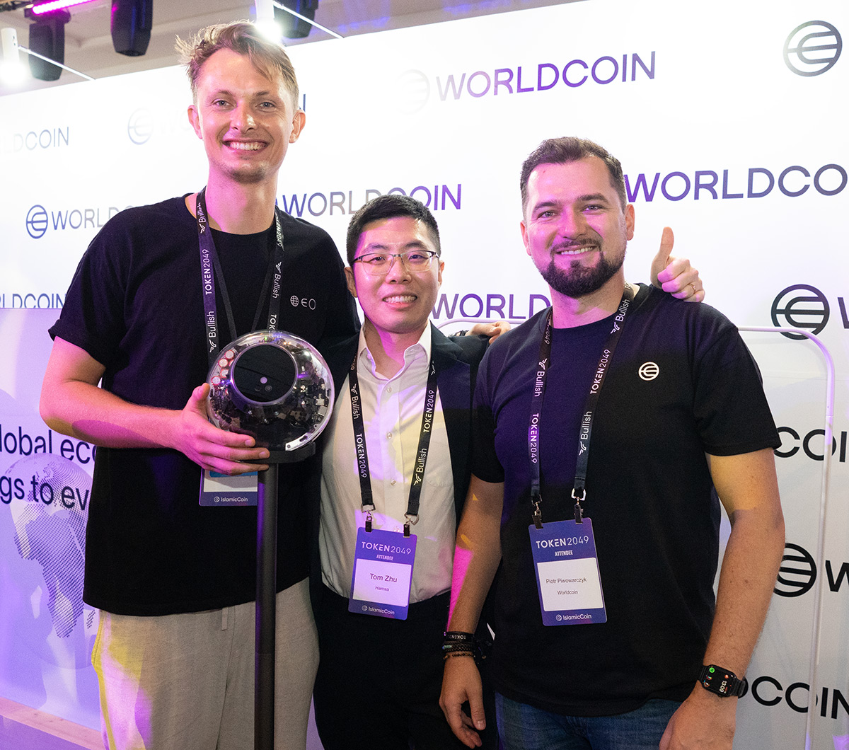 Three people at a Worldcoin event, one holding an Orb, smiling and engaging with each other.