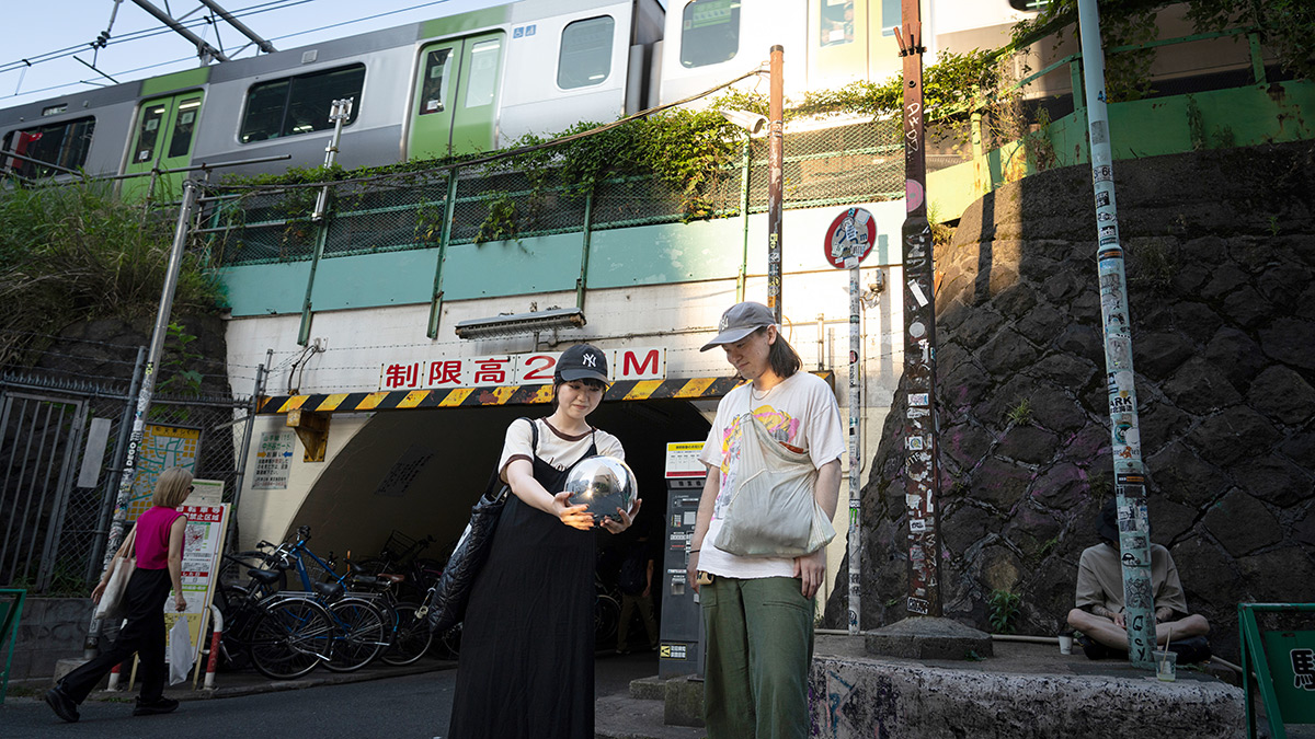 Two people using the Orb near a train station, with bicycles parked nearby and a train in the background.