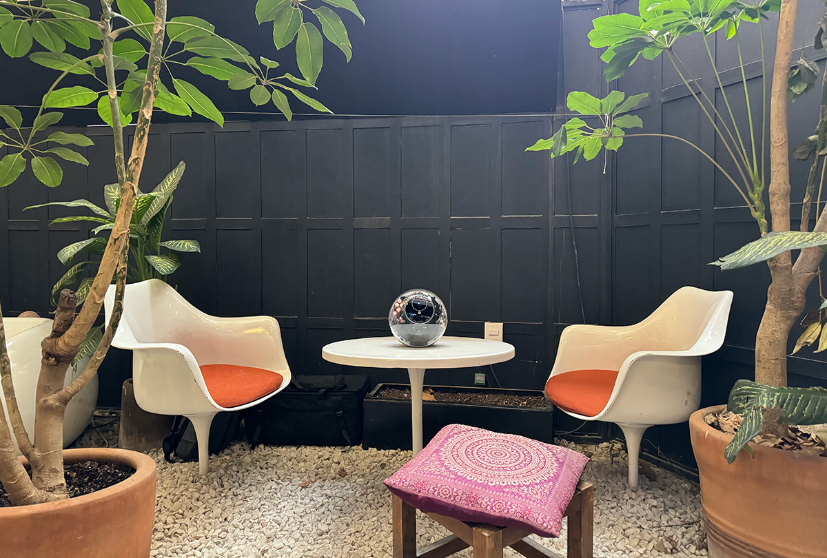Cozy seating area with two white chairs, a small table, and an Orb placed on the table, surrounded by greenery.