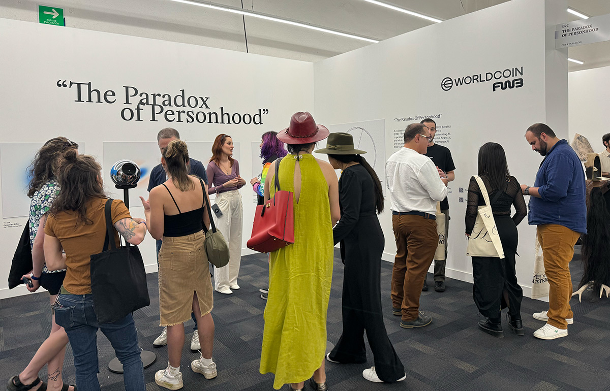 A group of people engaging in a discussion at an exhibition titled 'The Paradox of Personhood,' featuring Worldcoin branding in the background.