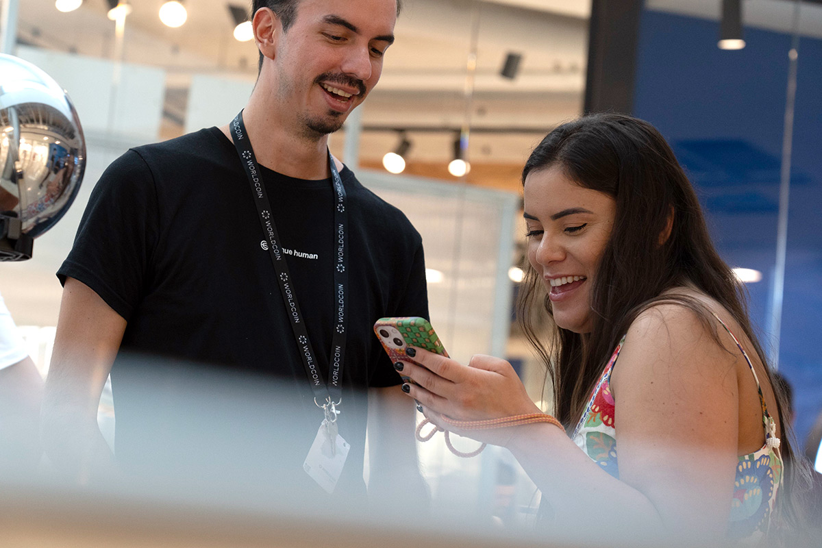 A smiling woman shows her phone to a man wearing a black shirt and a lanyard, both engaged in conversation near the Orb.