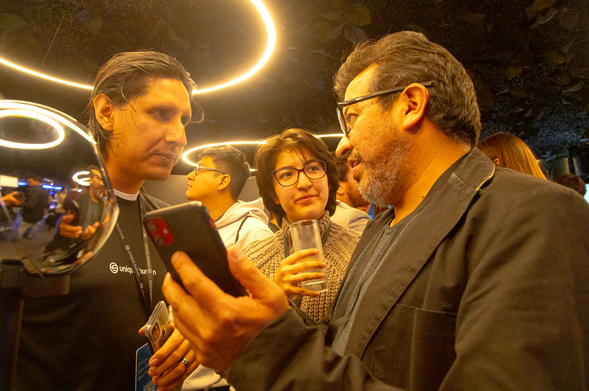 A group of people at an event engaging in conversation, with one person holding a smartphone and another using the Orb for verification.