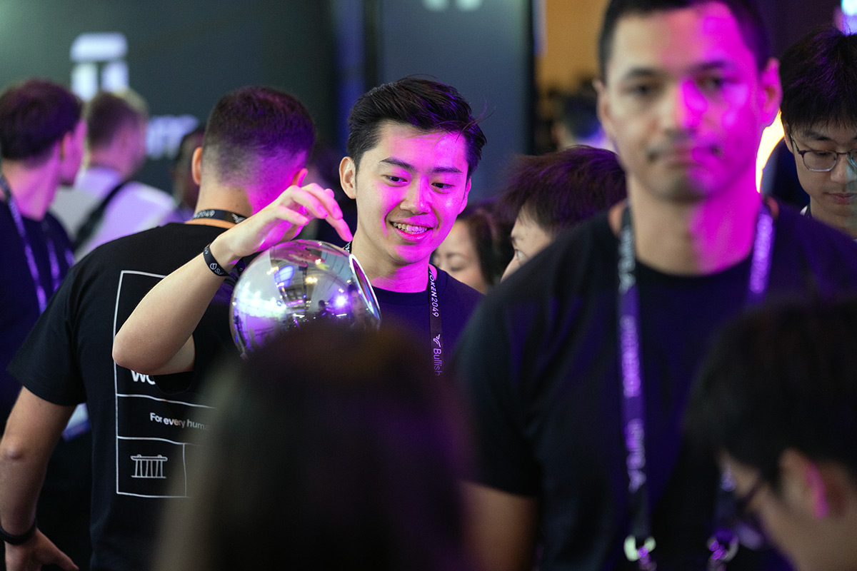 A young man joyfully verifying his identity using an Orb in a vibrant crowd at an event.