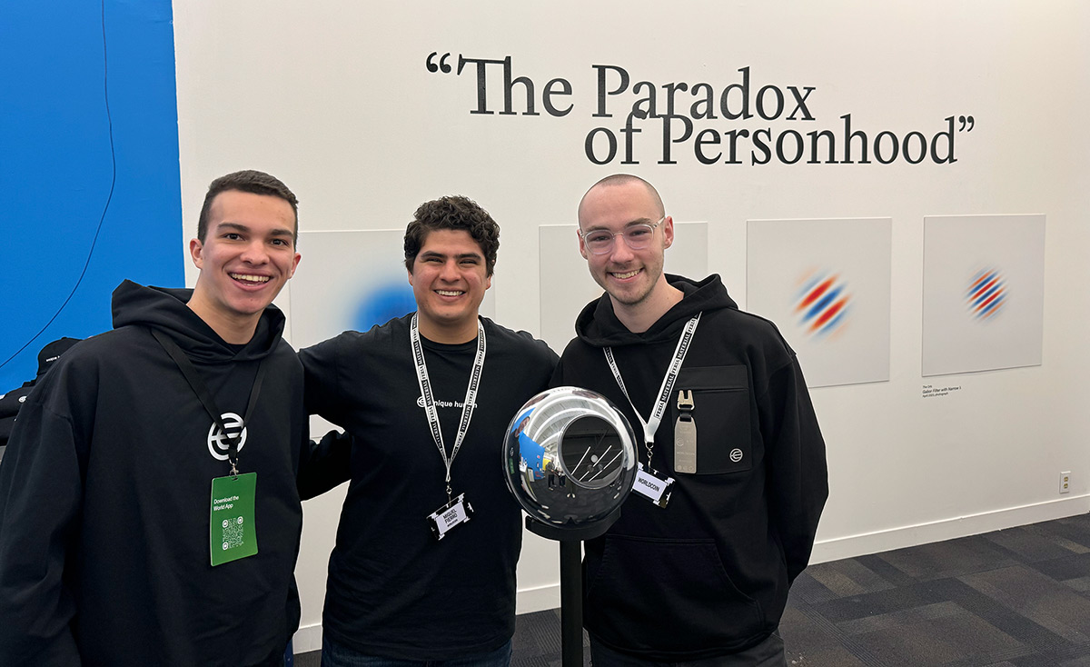 Three individuals smiling and posing together next to the Orb, with an exhibit backdrop displaying the phrase 'The Paradox of Personhood'.