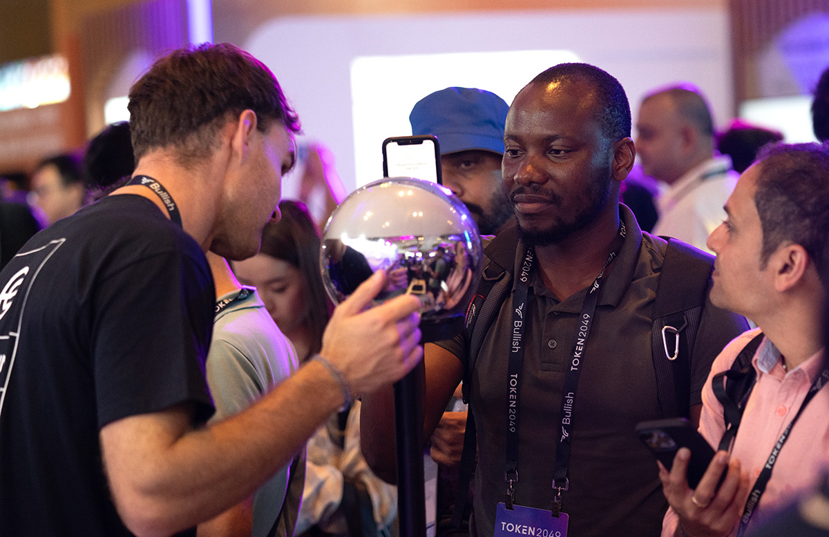 A crowd at an event with participants engaging around a spherical Orb for biometric verification. One person is focused on the Orb while others observe and interact.