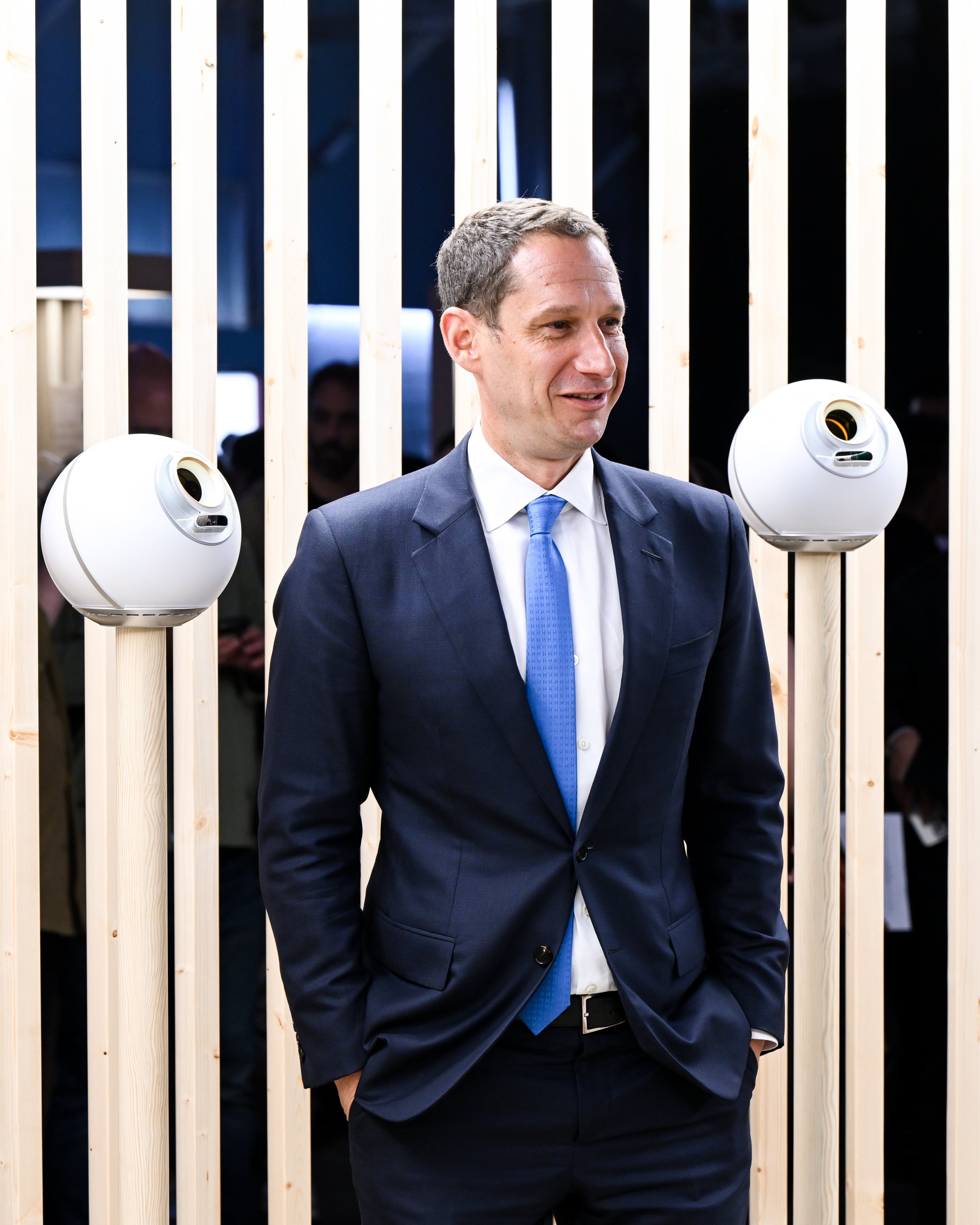 A man in a suit stands between two Orbs, showcasing technology at the World storefront launch in San Francisco's Union Square.