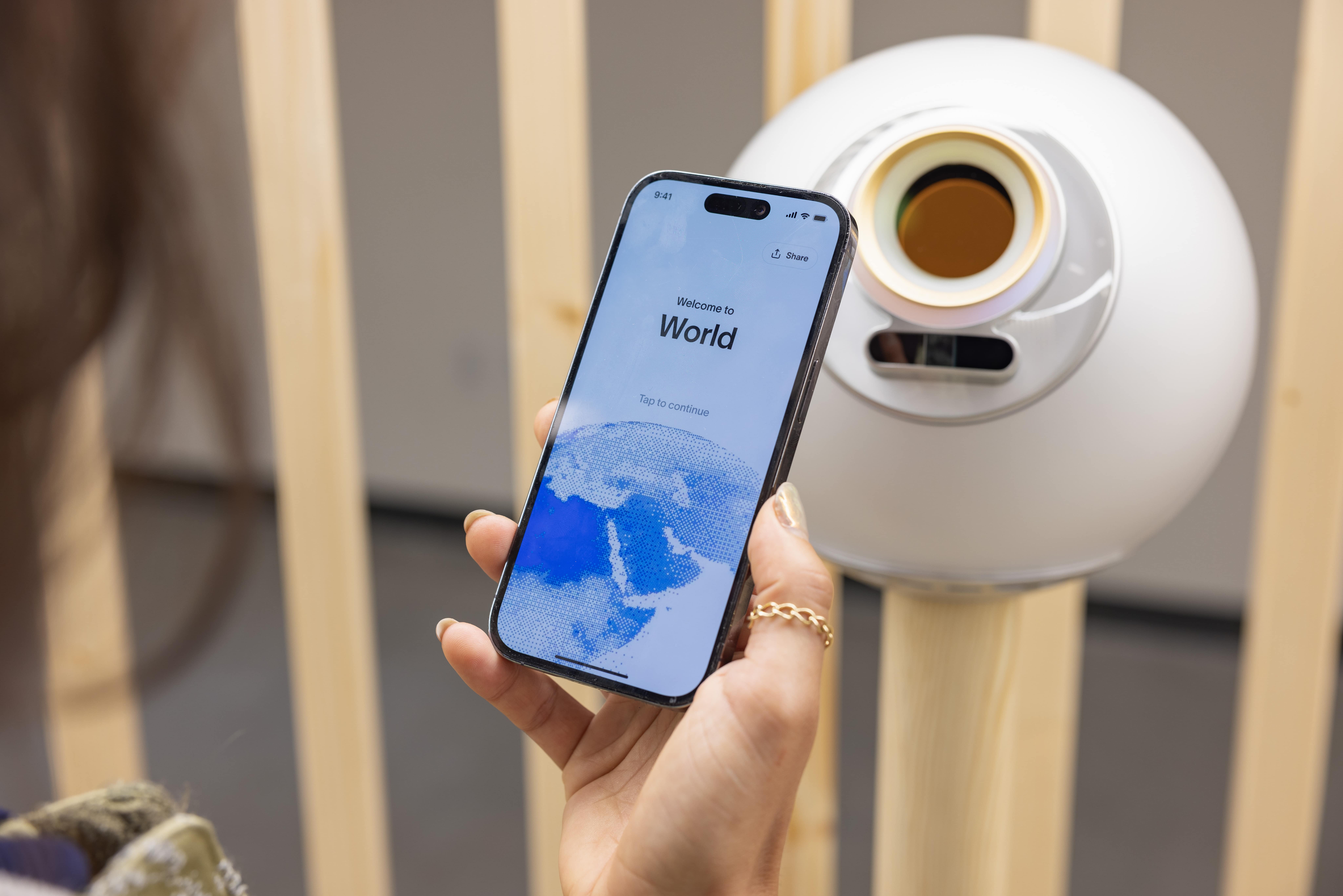 A person using a smartphone to access the World app in front of an Orb device.