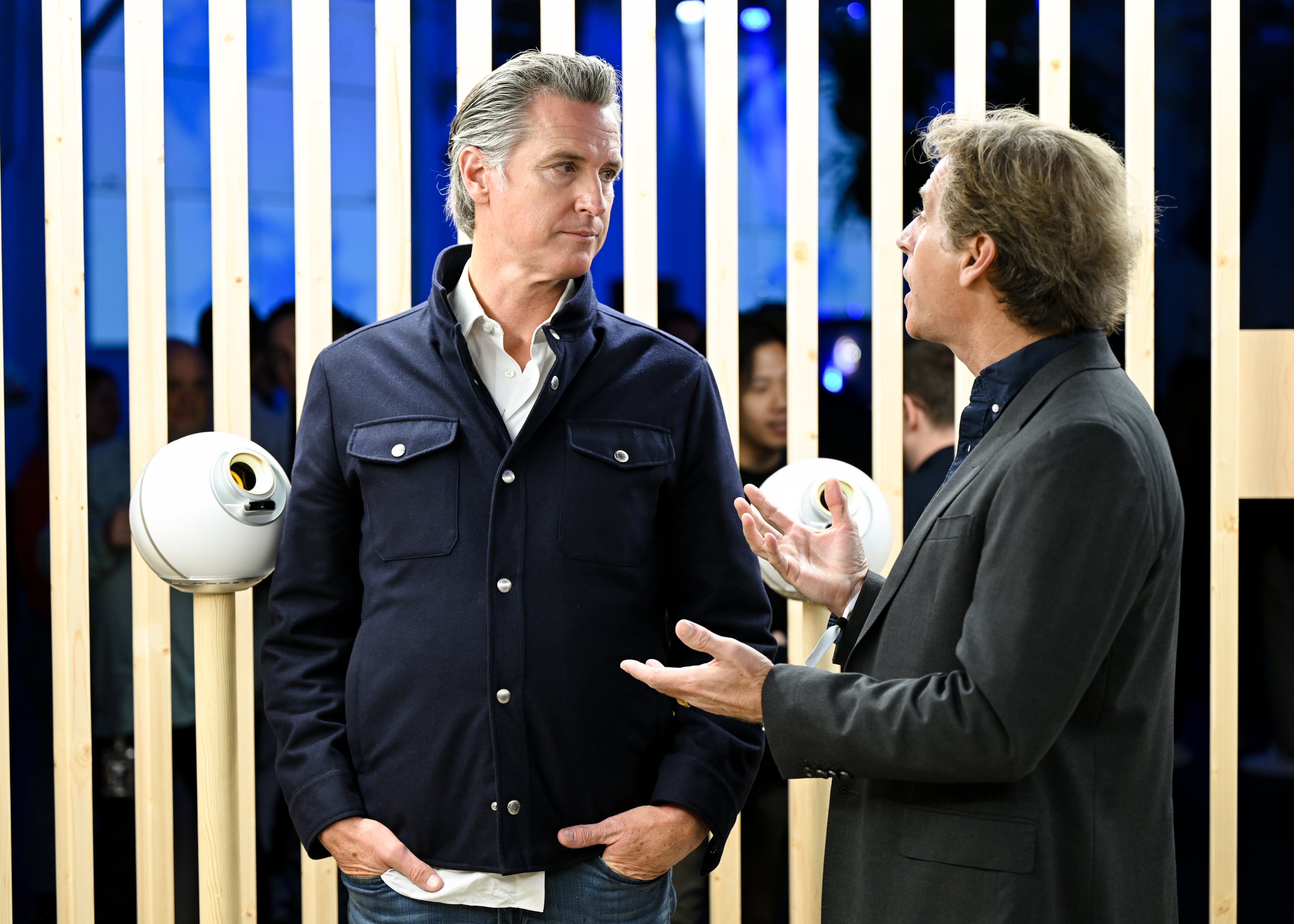 Two individuals engaged in conversation at a World event, with Orbs in the background.