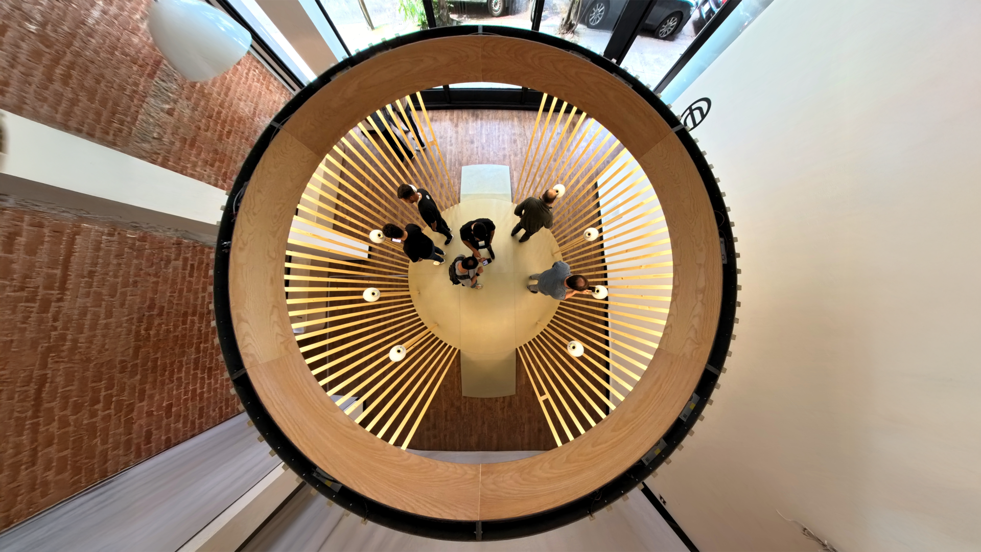 Aerial view of a circular wooden structure with people gathered around a central table, illuminated by soft lights.