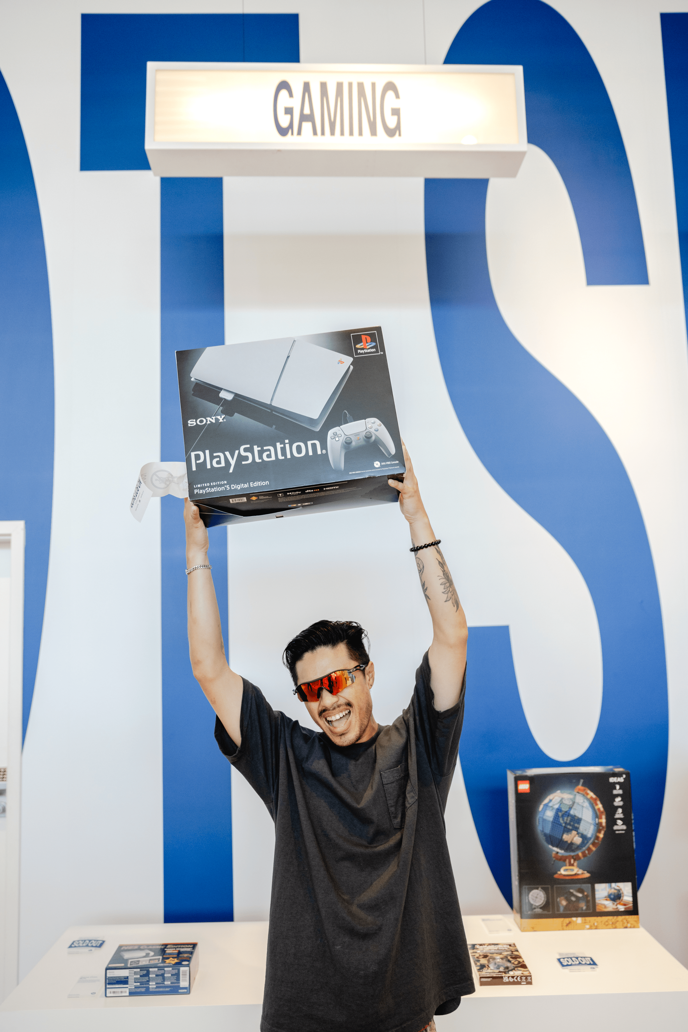 A person joyfully holds up a PlayStation console box, celebrating in a gaming-themed environment.