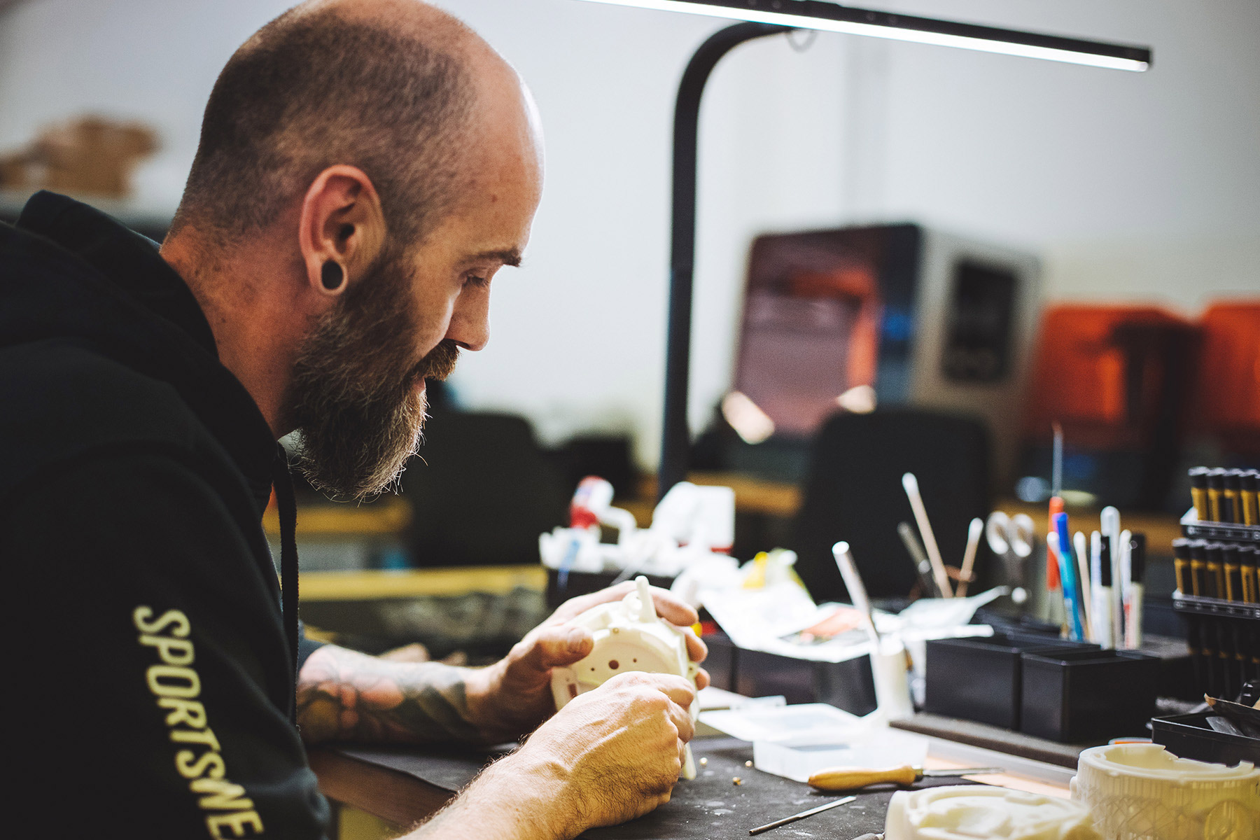 A person with a beard and earrings is focused on crafting or working with materials at a well-lit desk, illustrating hands-on engagement in innovative technology.
