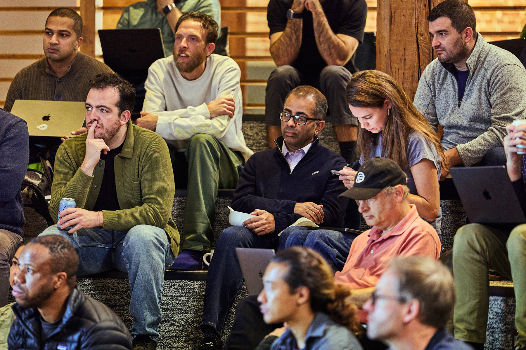 A diverse group of people engaged in a discussion or presentation, sitting on steps and using laptops in a collaborative environment.