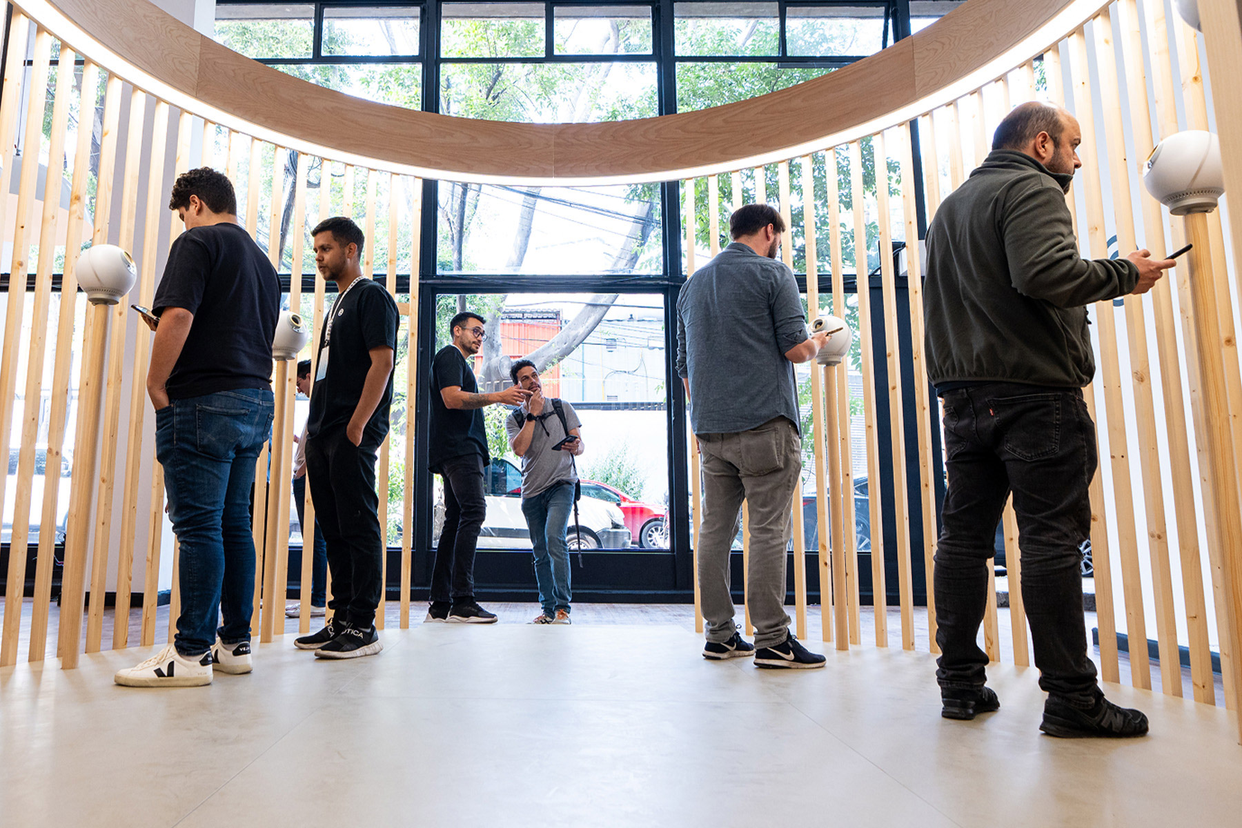 A group of individuals engaging with the Orbs in a modern, well-lit space, lined with wooden structures. Some are verifying while others use their phones, all contributing to an atmosphere of community and innovation.