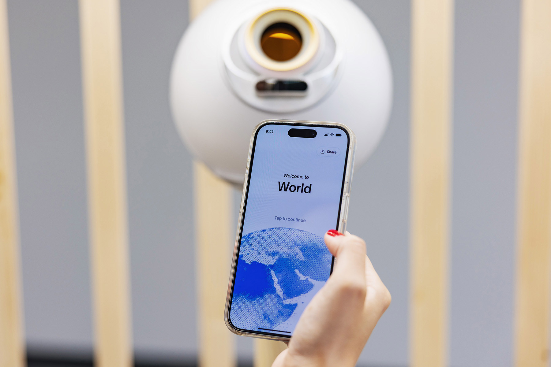 A smartphone displaying the World App interface in front of an Orb for biometric verification.