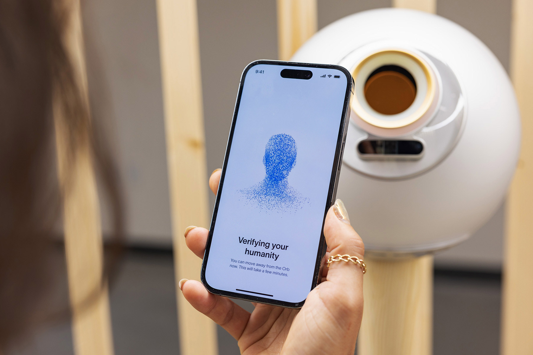 A person using a smartphone showing the World App interface while interacting with the Orb for verification.