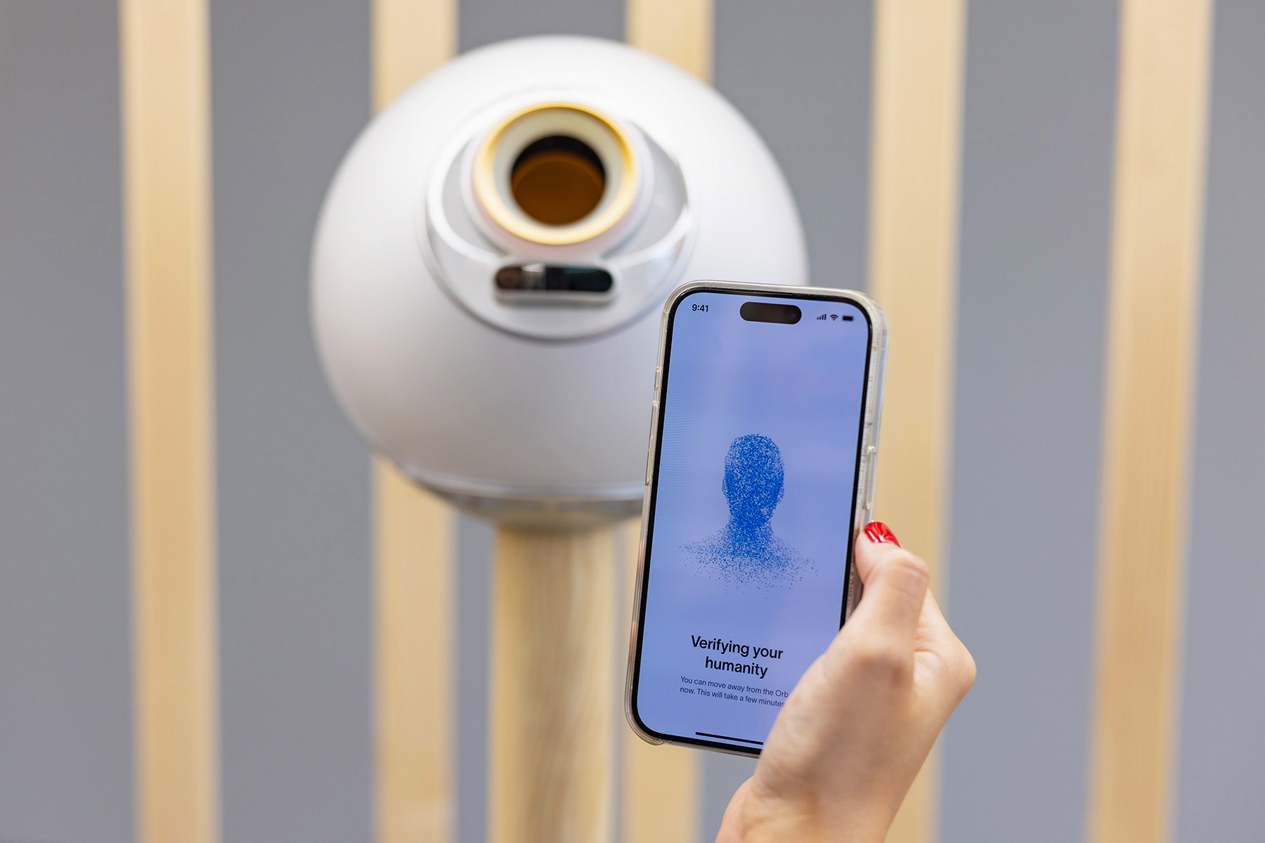 A user verifying their identity with a smartphone displaying the World App in front of an Orb.