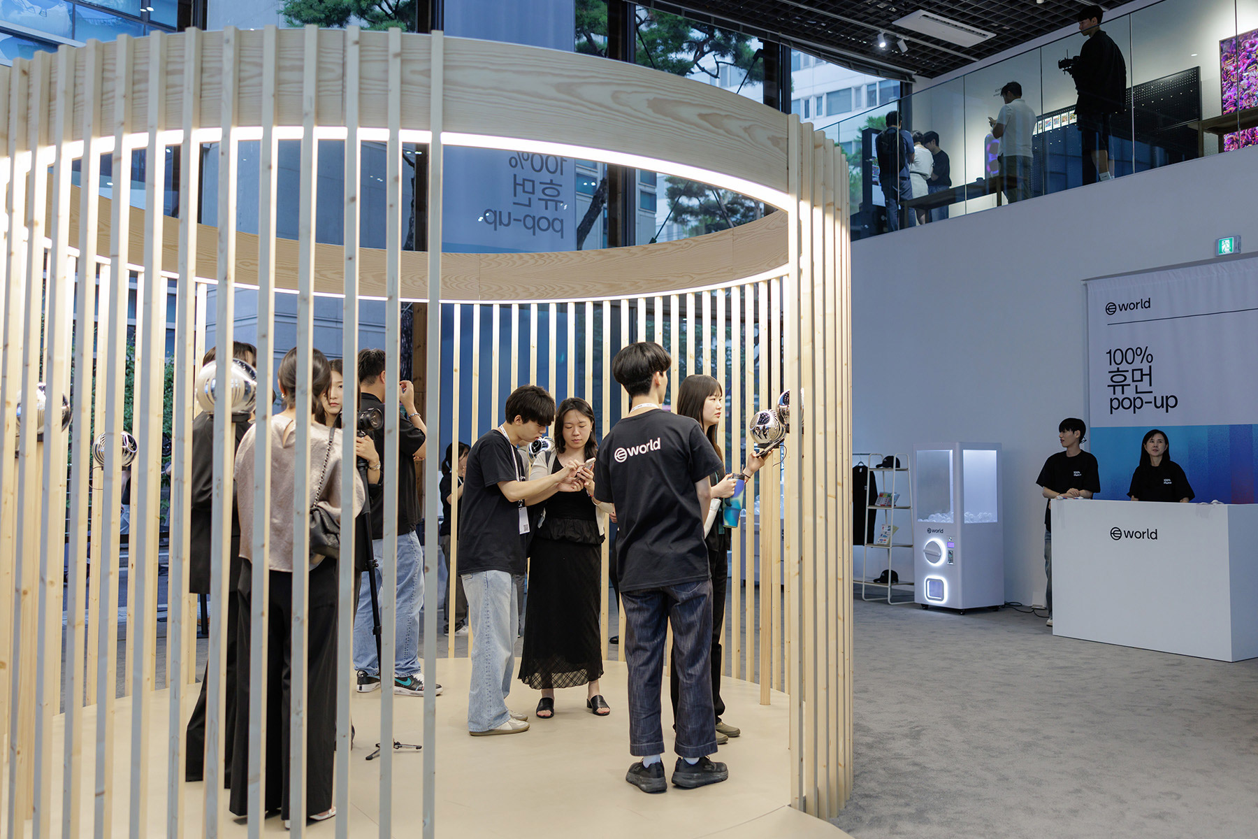 A group of people interacting with the Orb in a wooden circular installation at a pop-up event for World, while others observe from above.