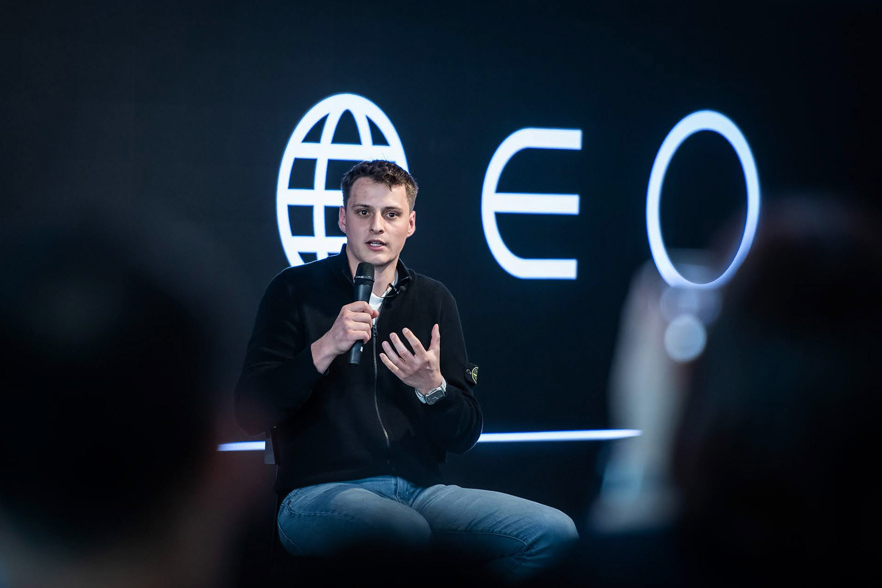 A speaker addressing an audience at a Worldcoin event, with a world logo displayed in the background.