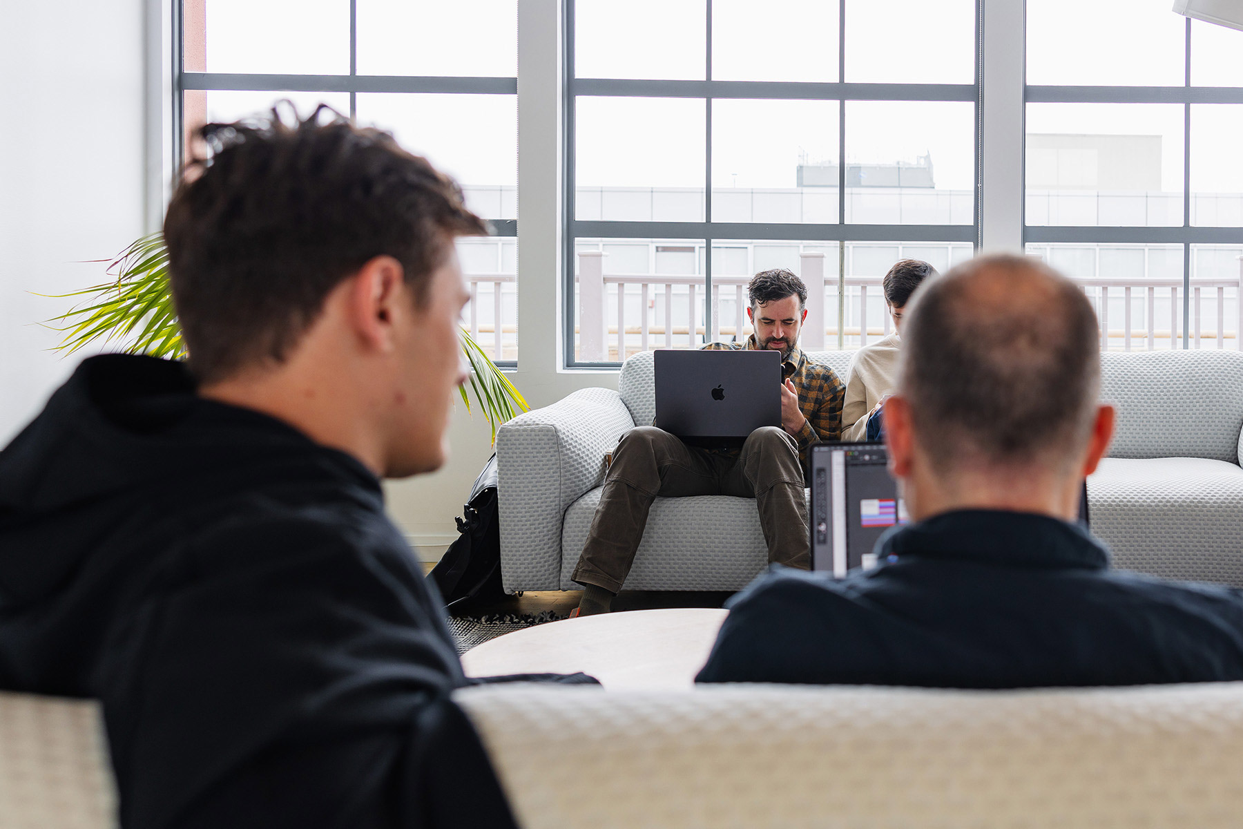 A group of people working collaboratively in a modern office space, with one person focused on a laptop while others engage in discussion nearby.