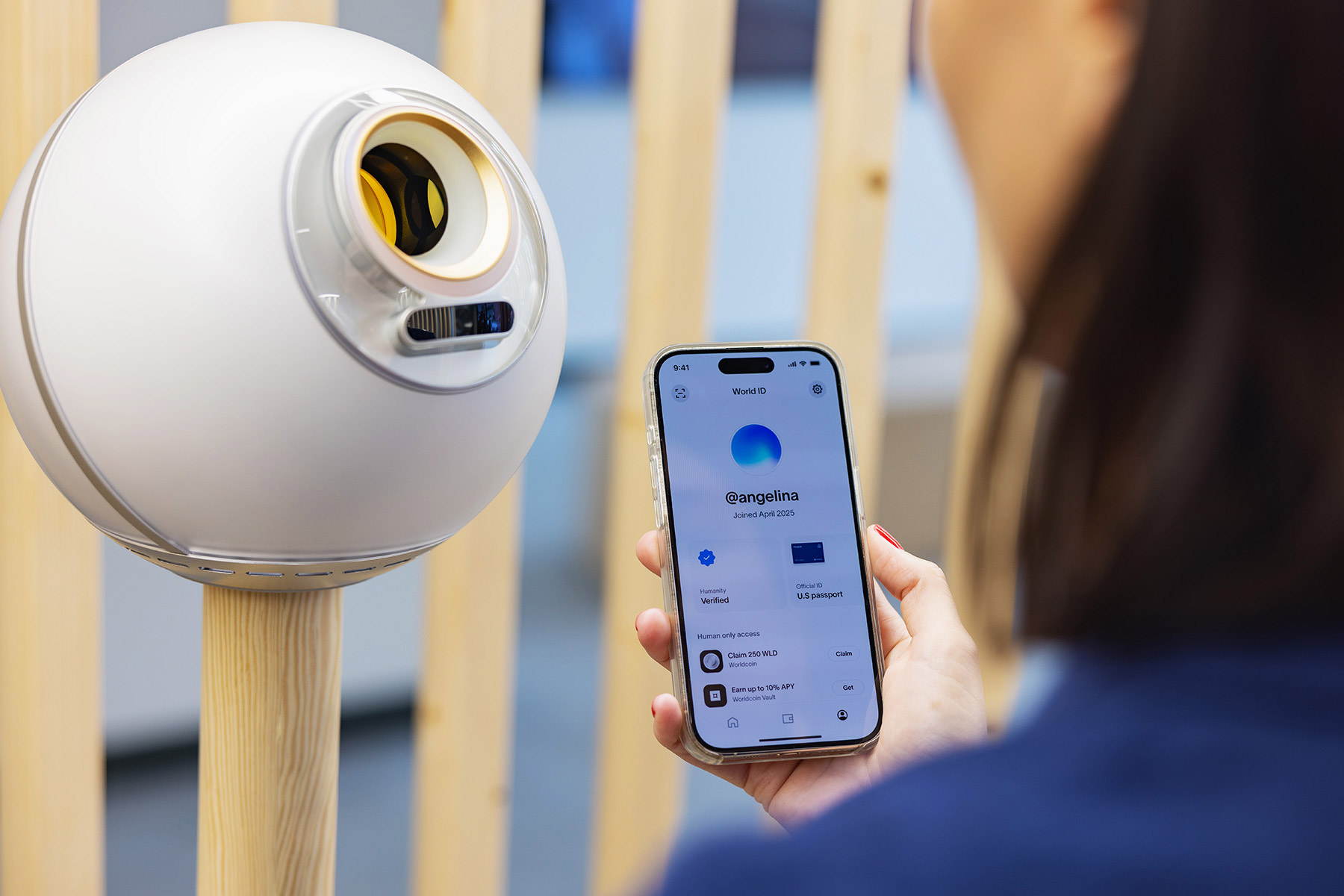 A person using a smartphone to access their World ID while interacting with an Orb for biometric verification.