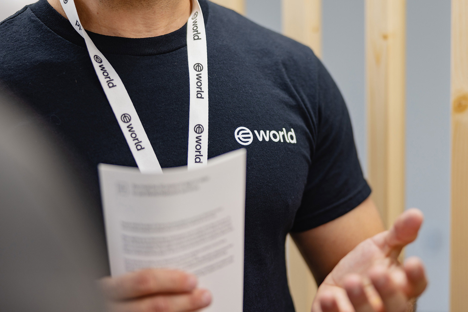 Person in a black shirt with World logo engaged in discussion, holding a document.