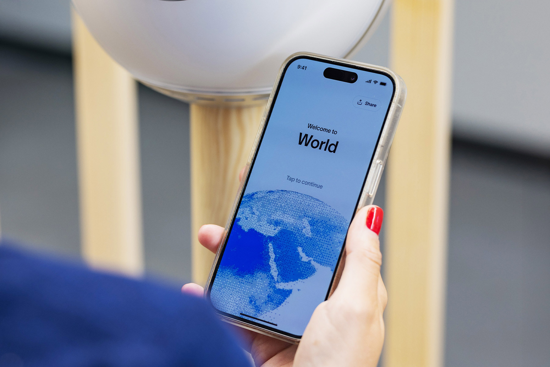 A smartphone displaying the World app welcome screen, with the Orb in the background.