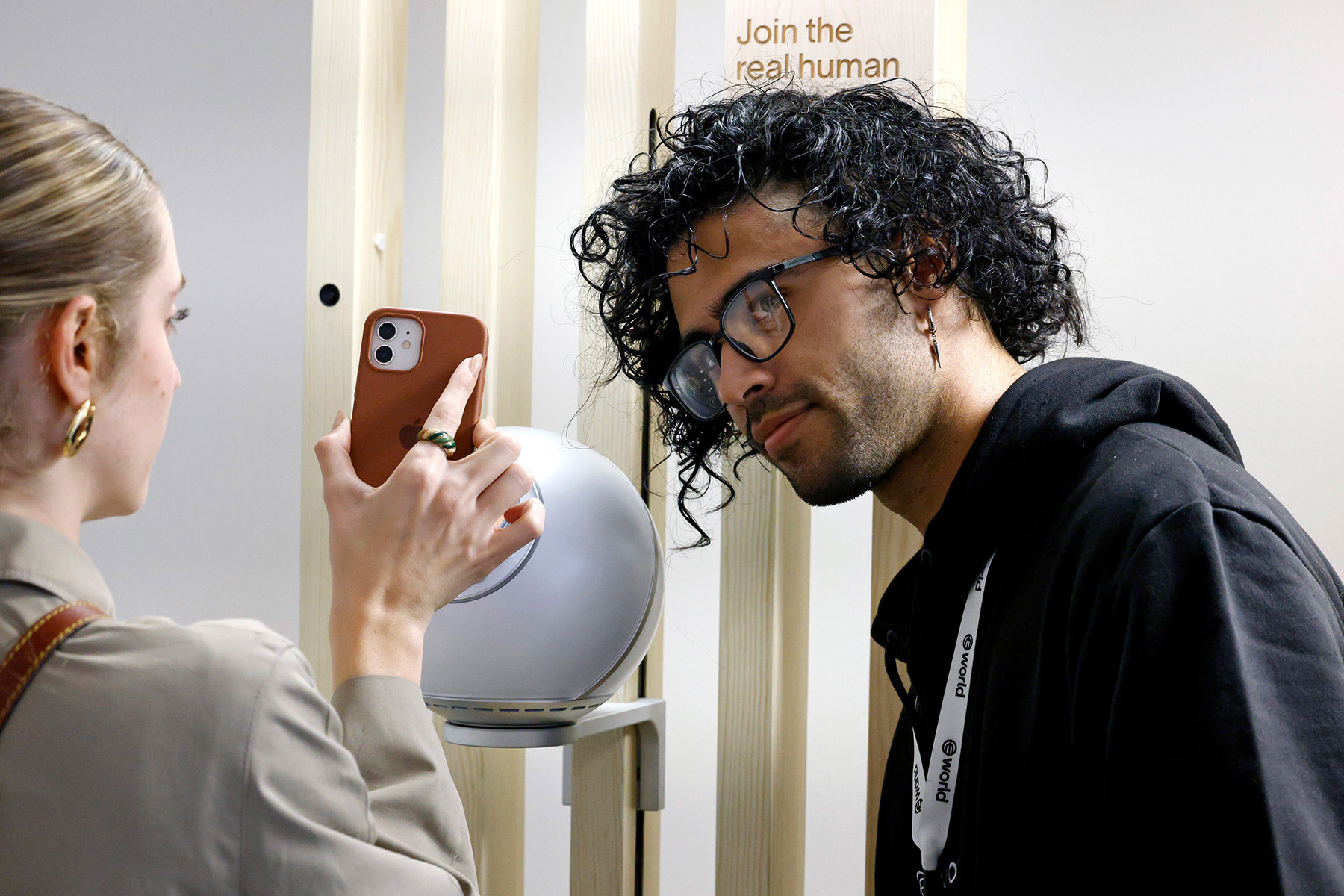 A person using a smartphone while another person interacts with the Orb, promoting digital identity verification in a welcoming space.