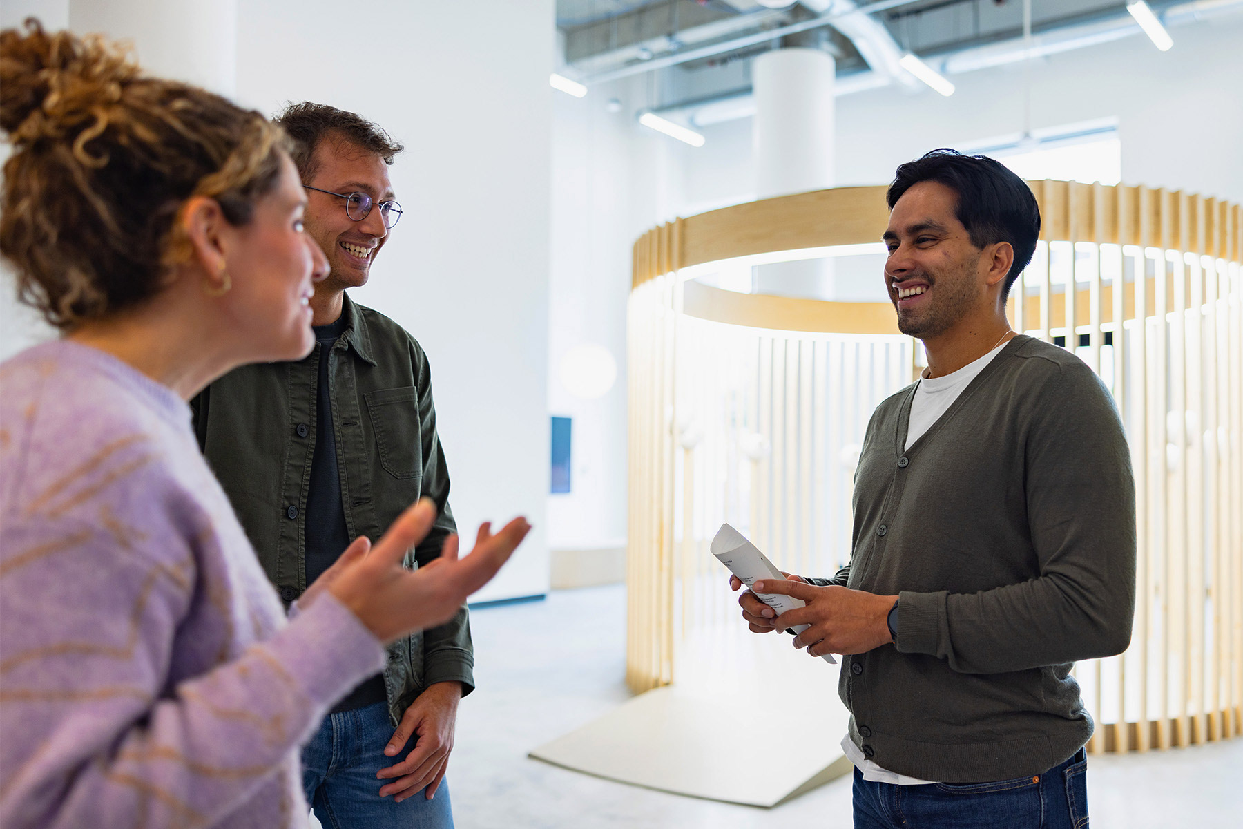 Three people engaged in a conversation, smiling and sharing ideas in a modern space. One person holds an Orb, symbolizing biometric verification.