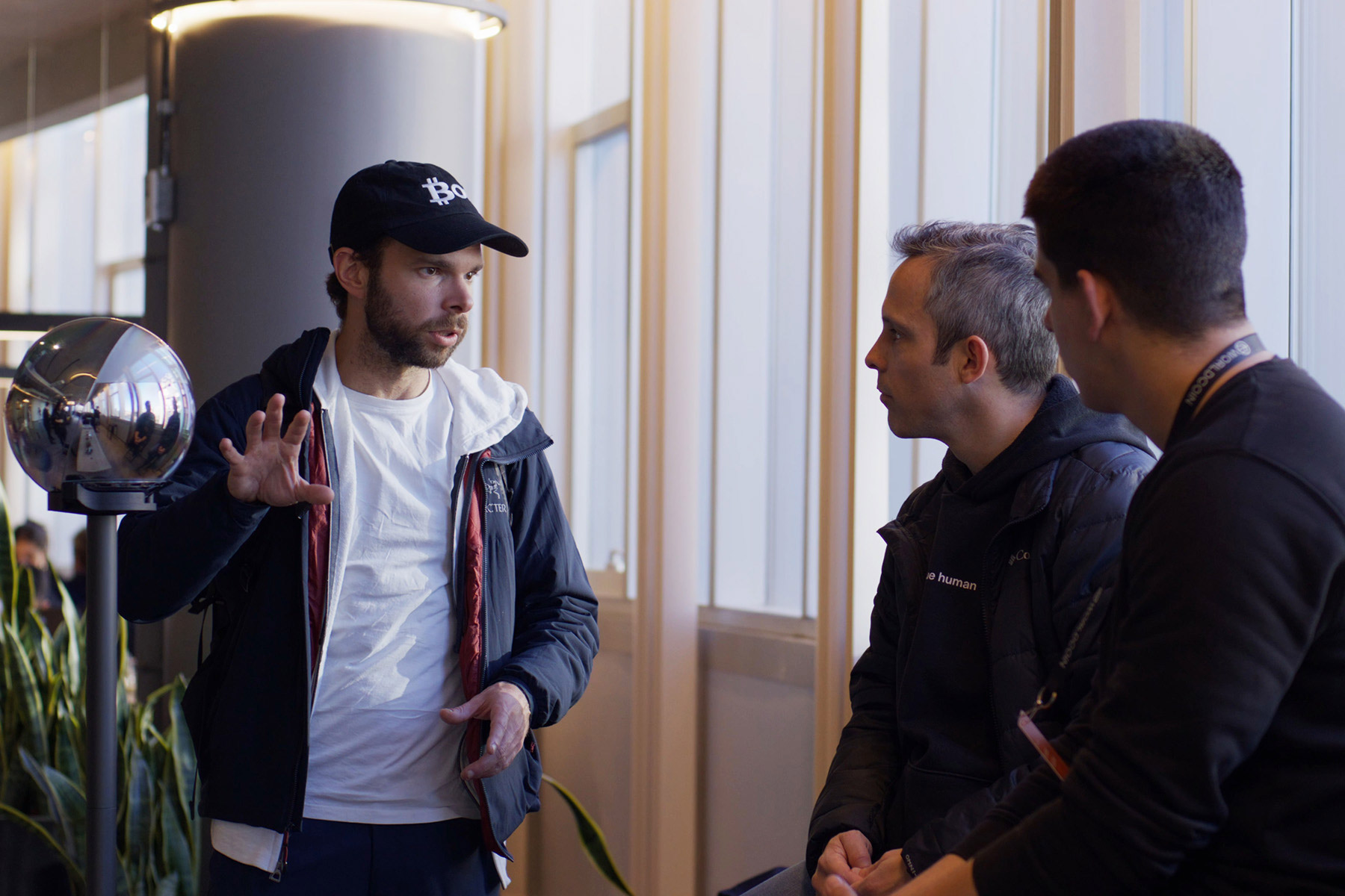 Three individuals engaged in conversation about the Worldcoin Community Grants Program, with the Orb in the background.
