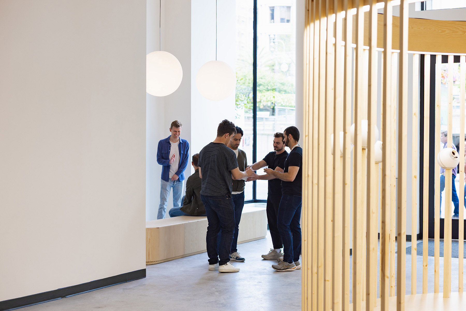 Group of people interacting in a modern indoor space, discussing and using devices. Bright and inviting atmosphere with large windows.
