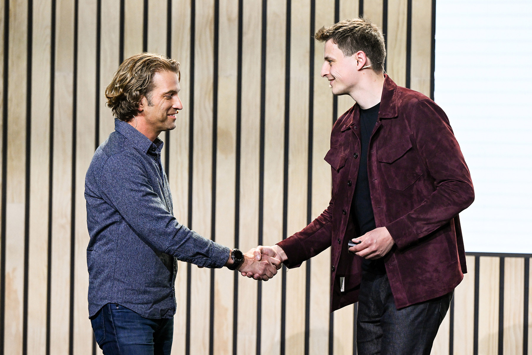Two individuals shaking hands on stage, symbolizing collaboration and innovation.