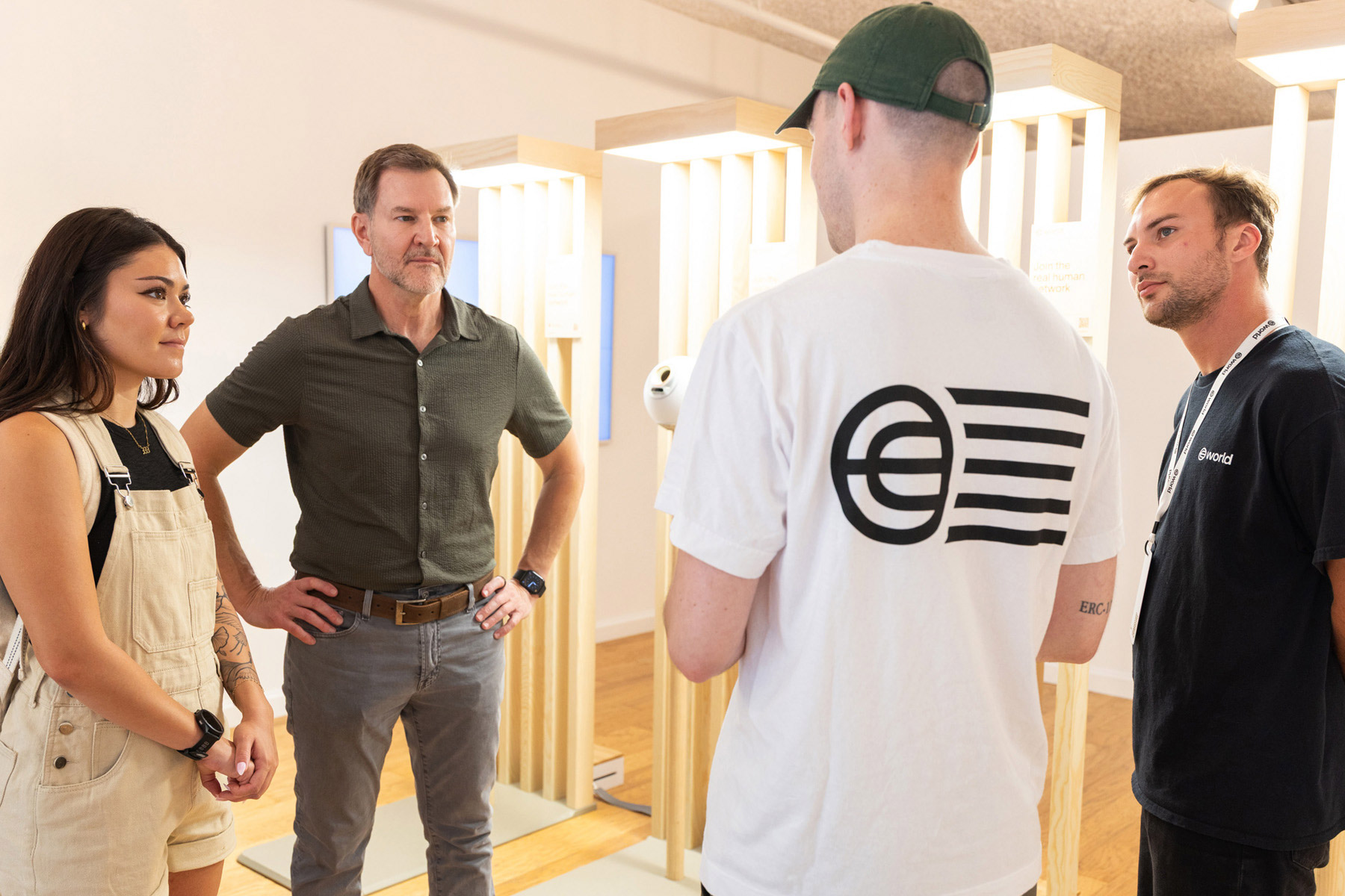A group of four individuals engaged in a discussion about World ID, with the Orb visible nearby as a symbol of biometric verification.