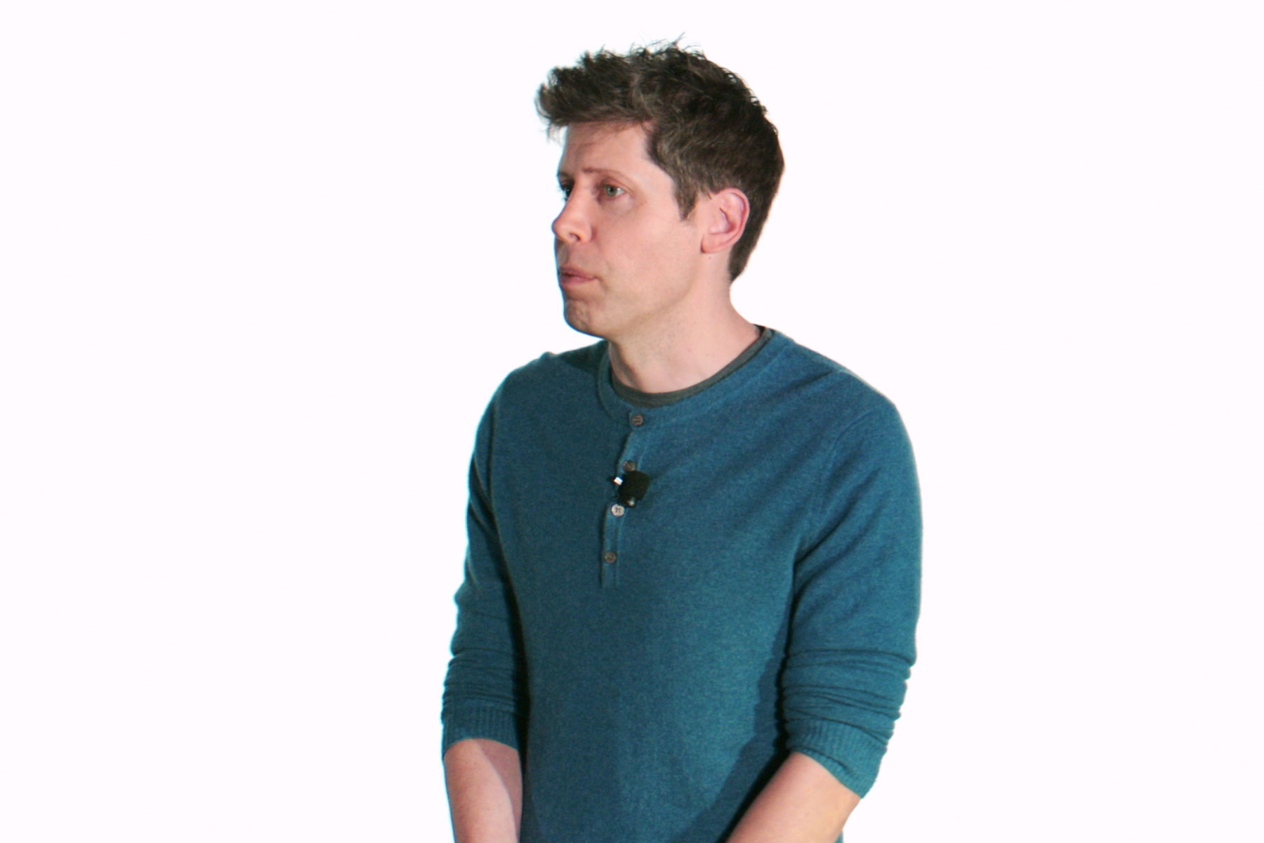 A person in a blue shirt speaking, against a plain background.