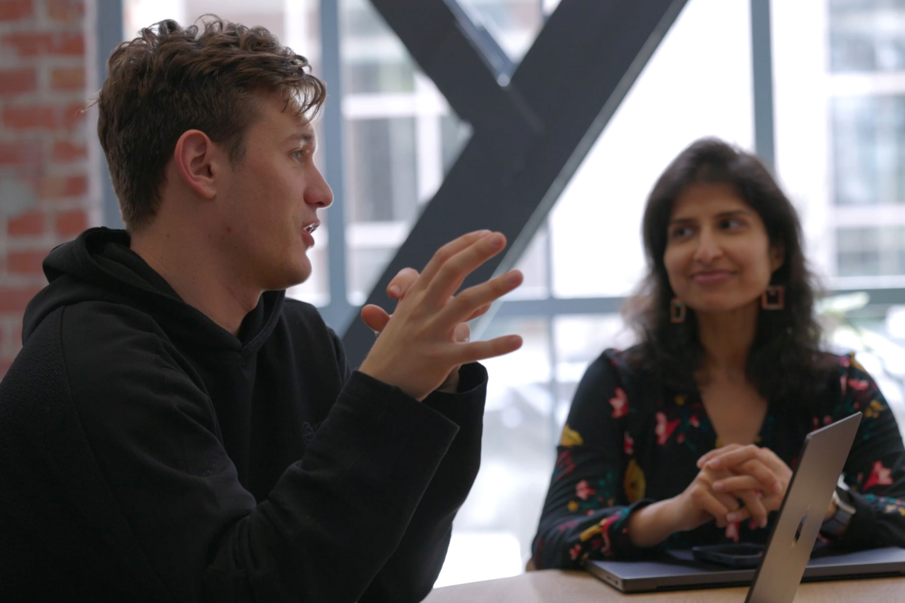 Two people in a meeting discussing strategies, with one gesturing and the other listening attentively, symbolizing collaborative efforts in responsible technology development.