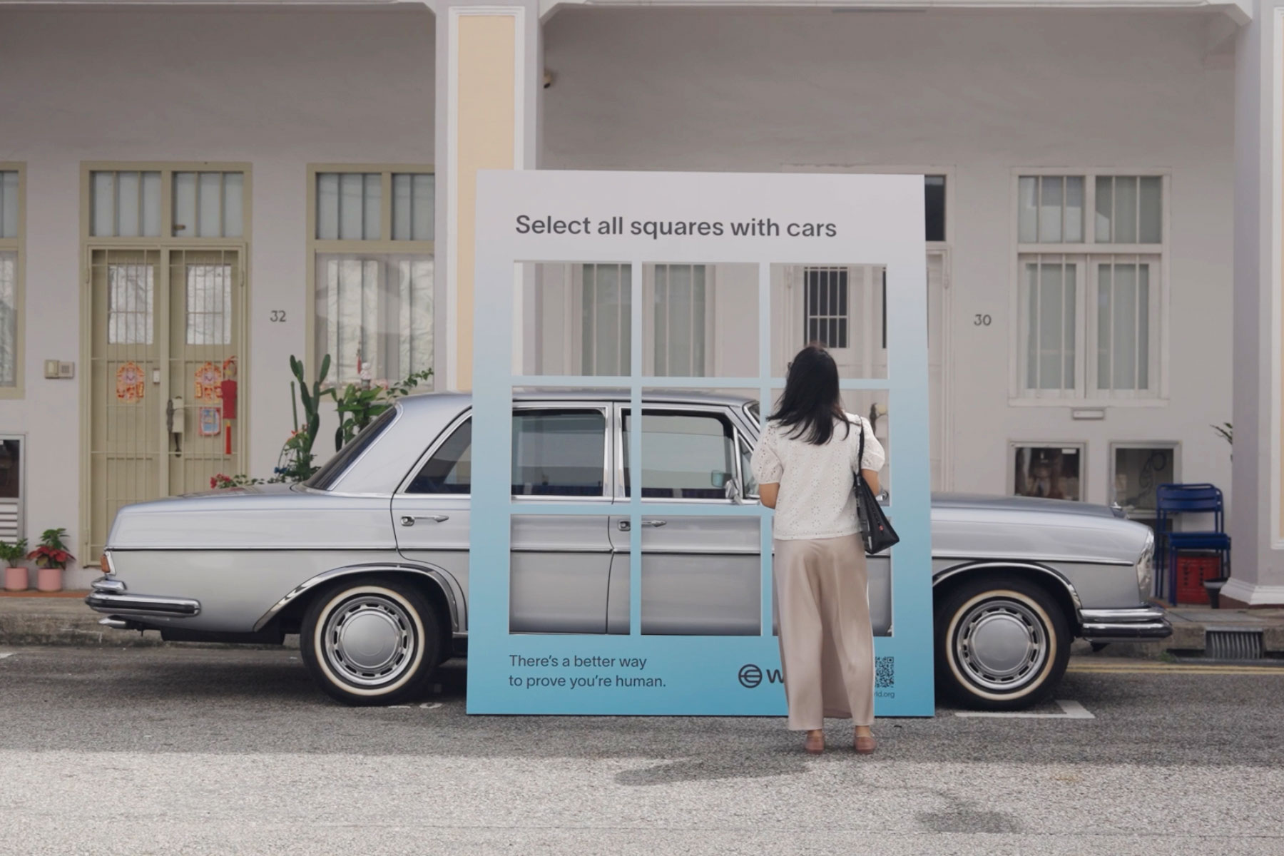 A person interacting with a display that prompts them to select squares containing cars, positioned in front of a classic silver car.