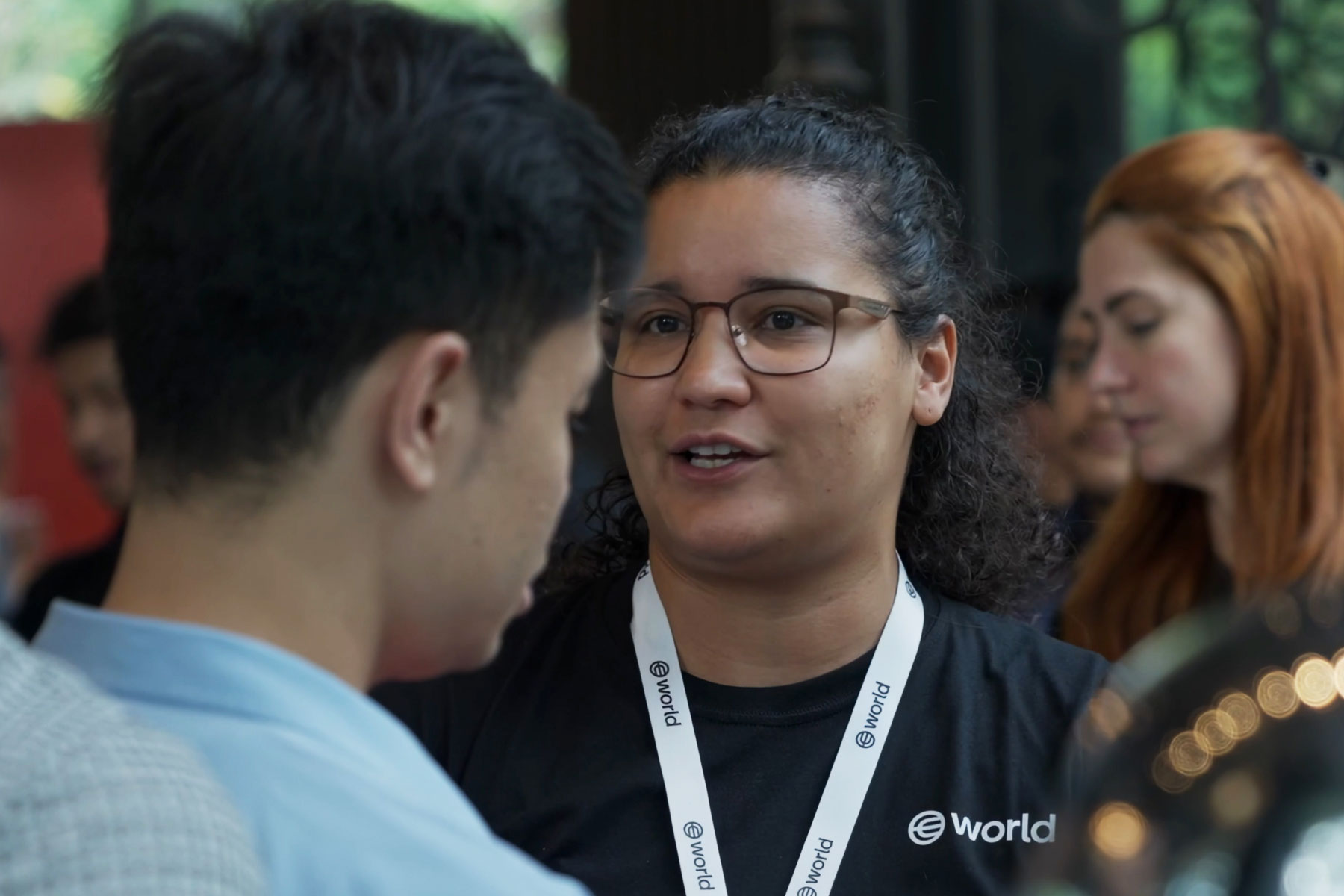 A person wearing a World t-shirt engages in conversation with another individual at an event.
