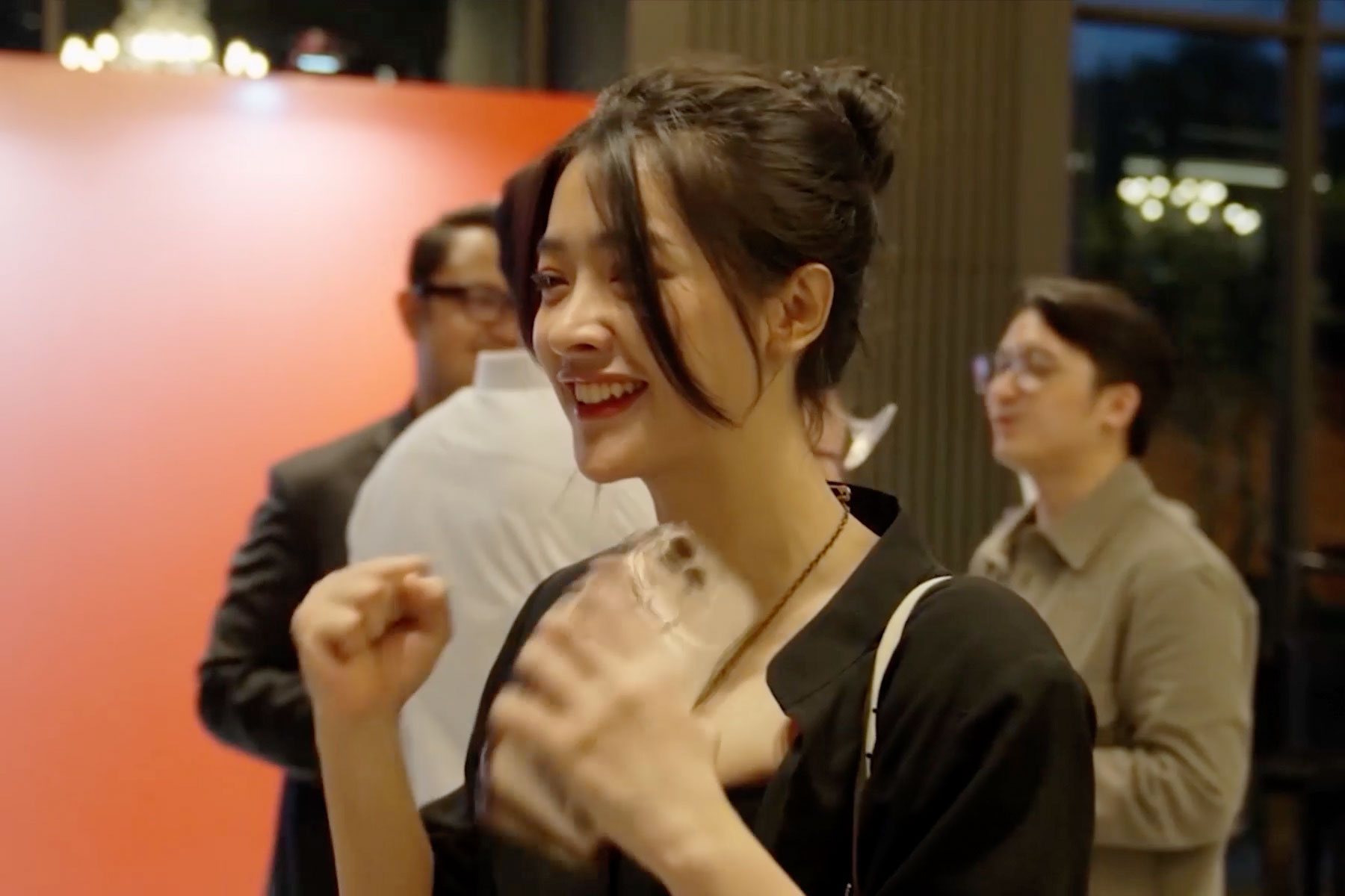 A woman smiling and engaging joyfully at an event, with others mingling in the background.