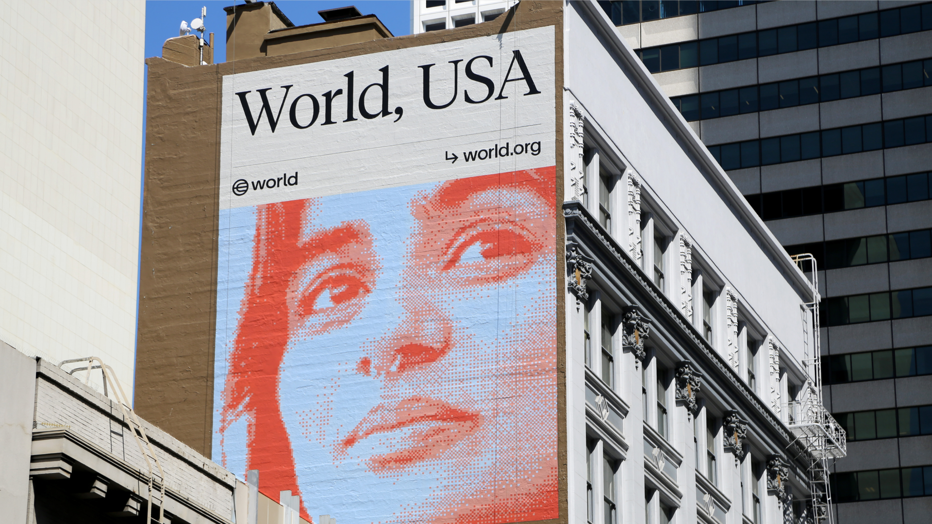 Mural przedstawiający zbliżenie twarzy kobiety, z napisem "World, USA" wyeksponowanym powyżej. Mural znajduje się na budynku w miejskim otoczeniu, prezentując żywe i angażujące dzieło sztuki.