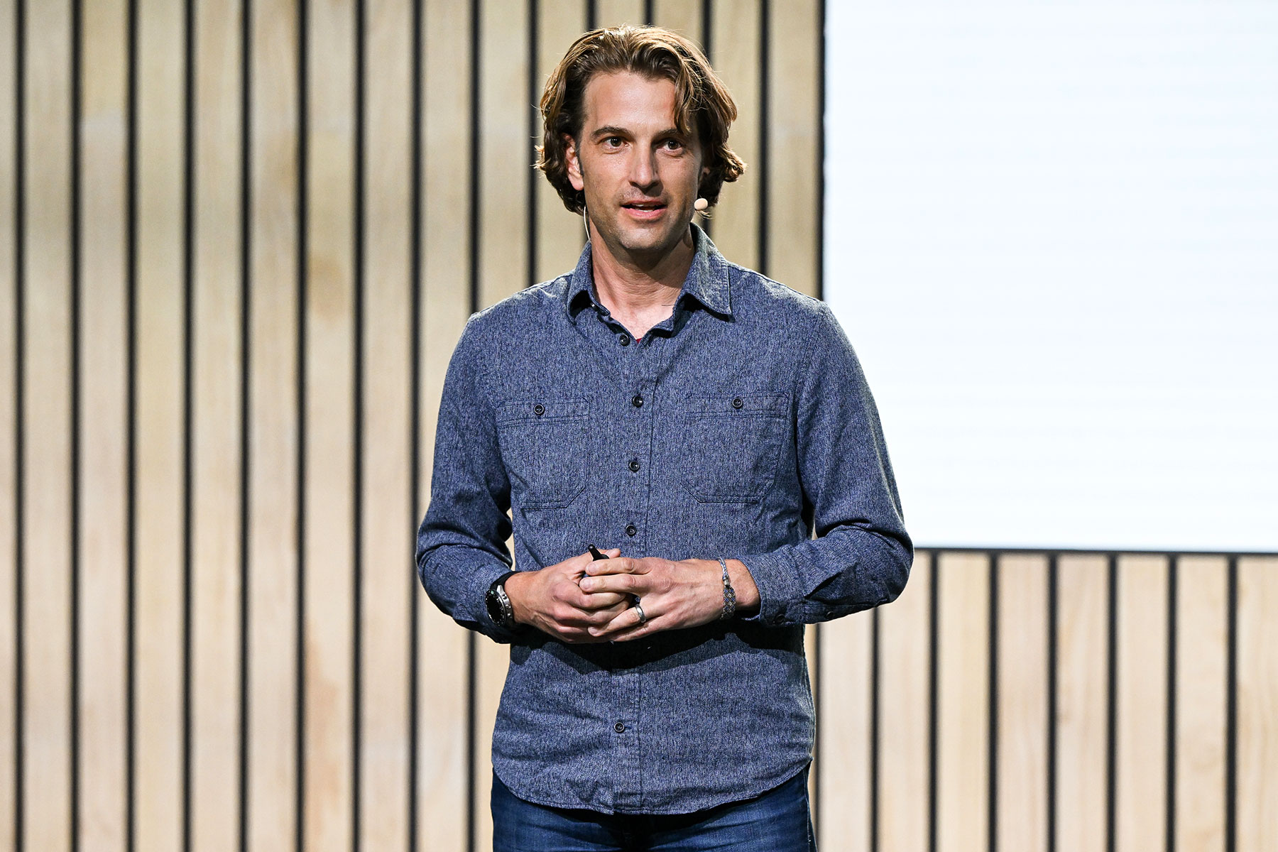 A speaker presenting on stage, discussing privacy in the age of AI, with a backdrop of wooden panels.